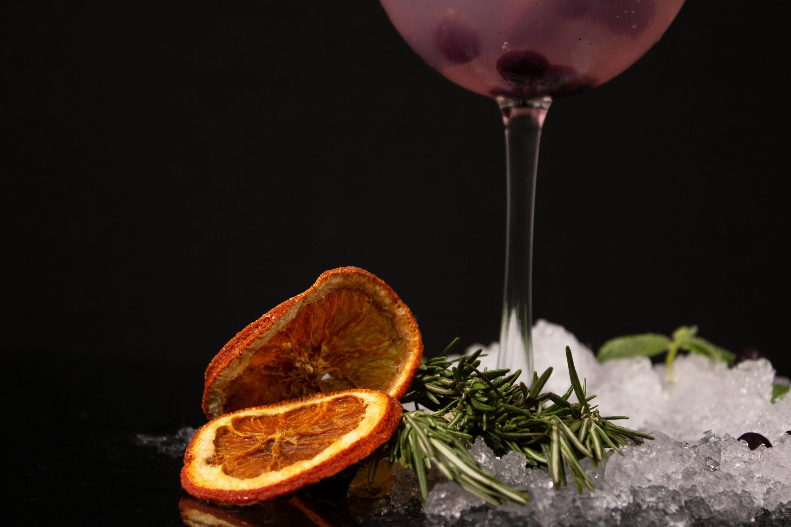 Close-up of a cocktail with dried orange slices and rosemary. Perfect for festive and culinary themes.